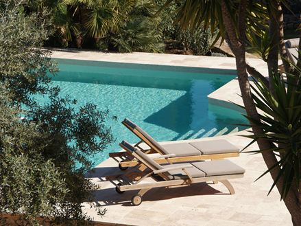 Deux transats au soleil au bord de la piscine. Au sol, des dalles en travertin beige Medium