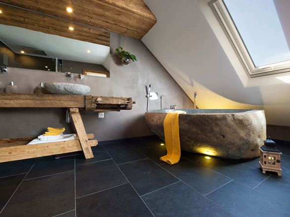 Salle de bain rustique avec baignoire en pierre et carrelage d'ardoise foncé comme revêtement de sol.