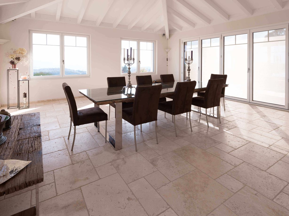 Salle à manger avec haut plafond, table et chaises sur travertin Light en assemblage romain