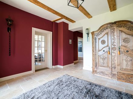 Pièce d´entrée sol en travertin mur rouge bordeau armoir en bois ur la droite et tapis bleu au sol